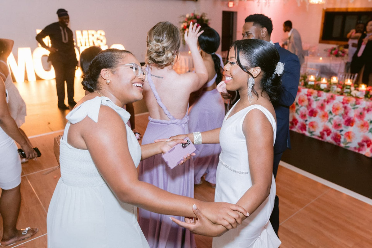 Two guests laughing and holding hands on a warmly lit reception dance floor