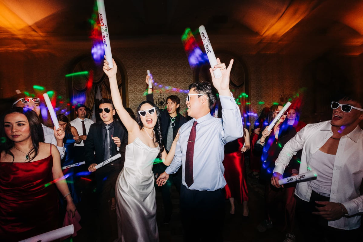 A wedding party dancing with arms up and light-up batons in a ballroom